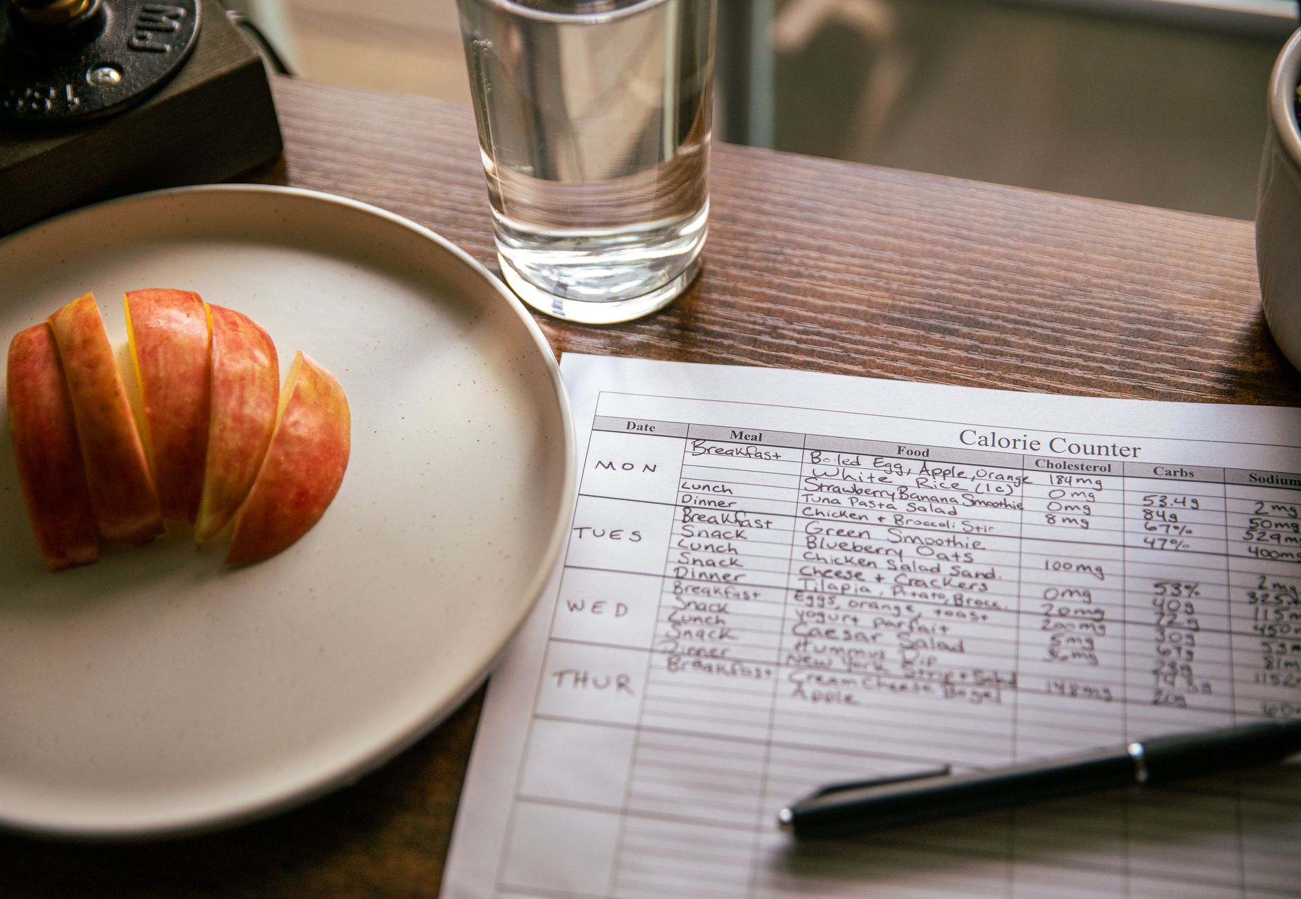 A table setup with apple slices, a calorie counting sheet, and a glass of water for a dieting scene.