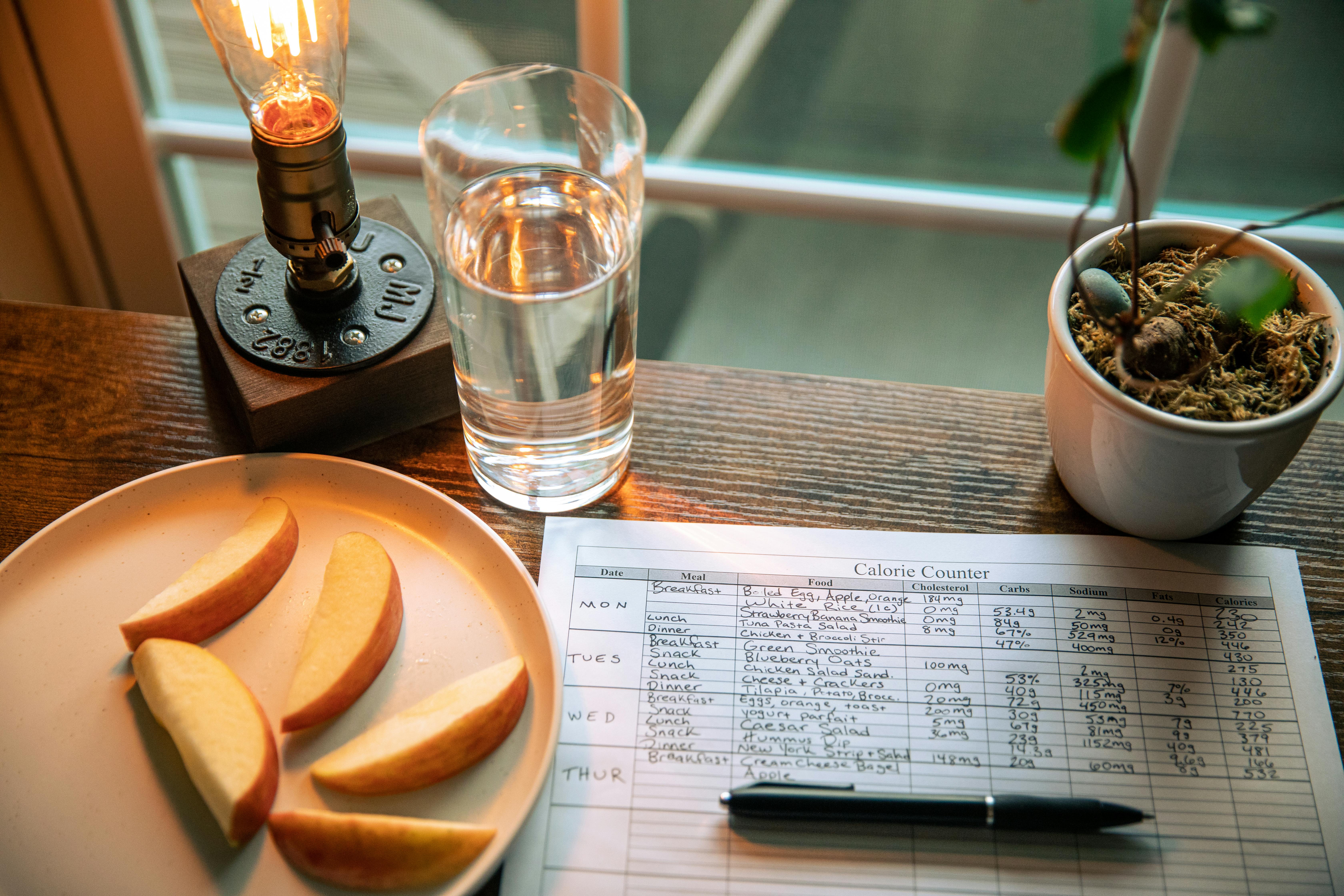 A cozy desk setup with apple slices, calorie counter, and water glass in warm lighting.