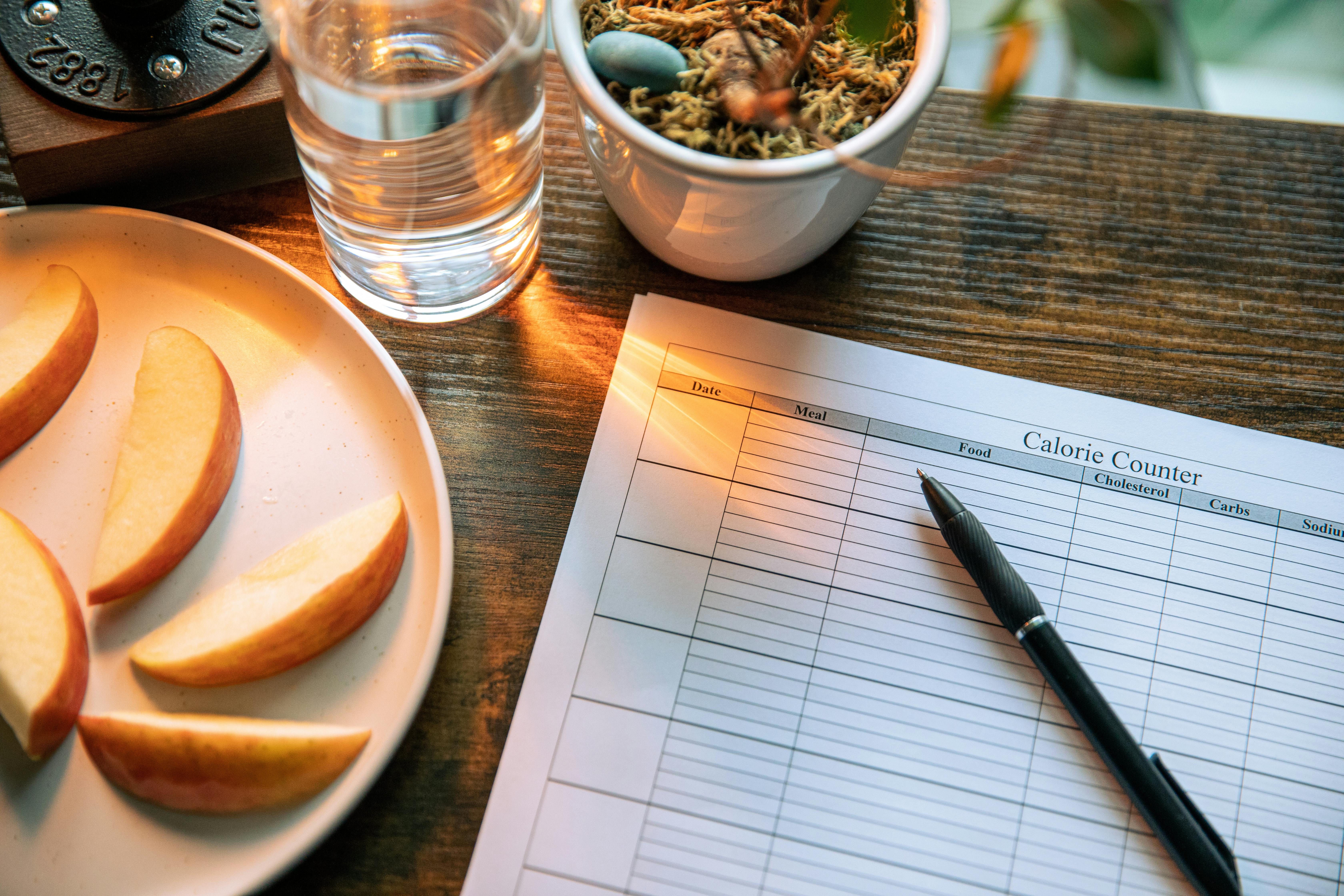 Calorie counting setup with apple slices and glass of water on a wooden table.