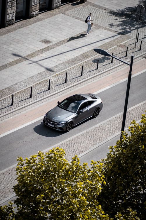Free A bird's-eye view of a sleek gray car driving down a city street, surrounded by trees and pavements. Stock Photo