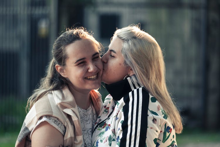 Blonde Woman In Adidas Floral Jacket Kissing Woman In White And Brown Vest