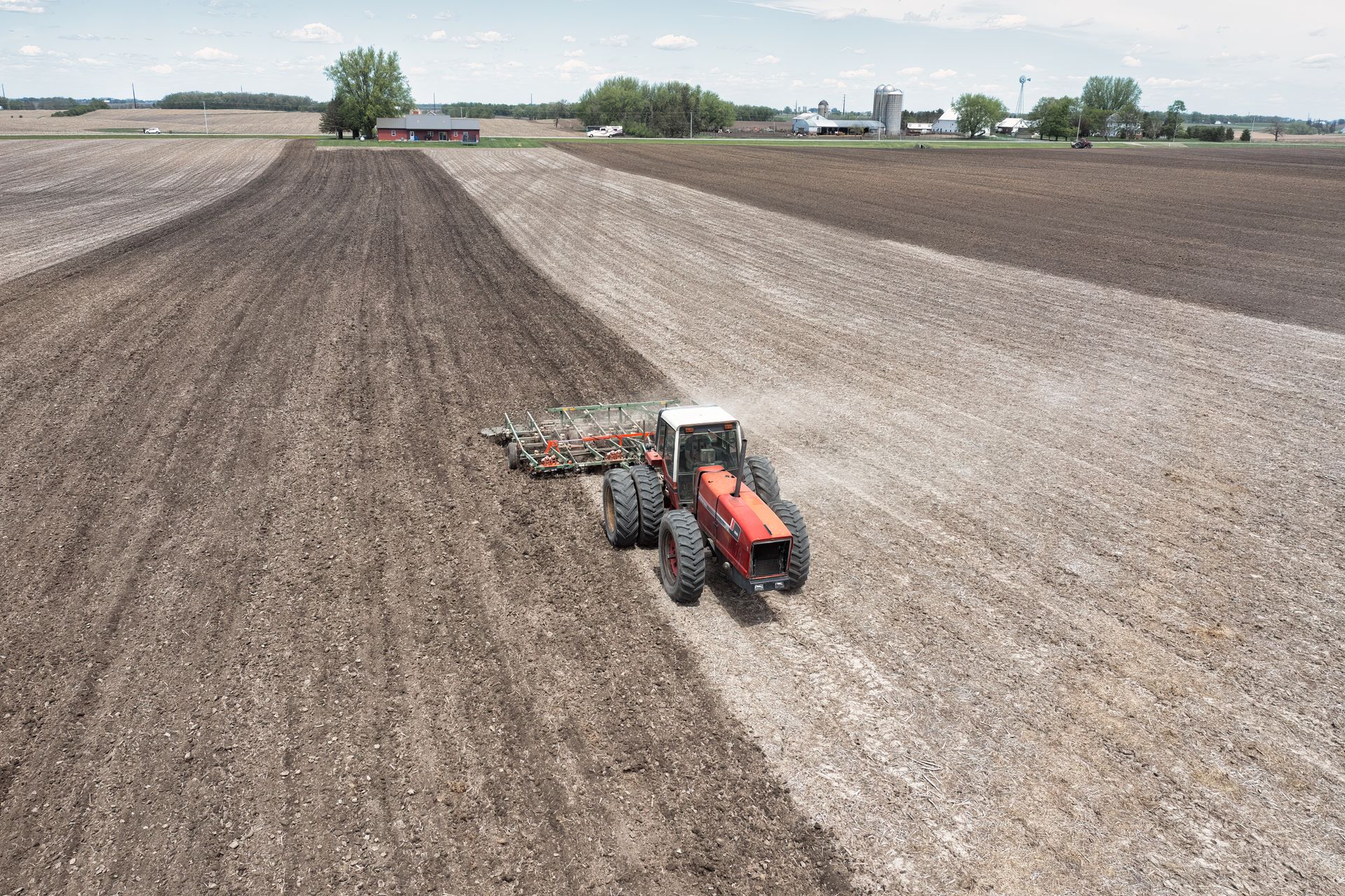 A drone captures a tractor plowing fields on a spring day, showcasing agriculture in Minnesota.