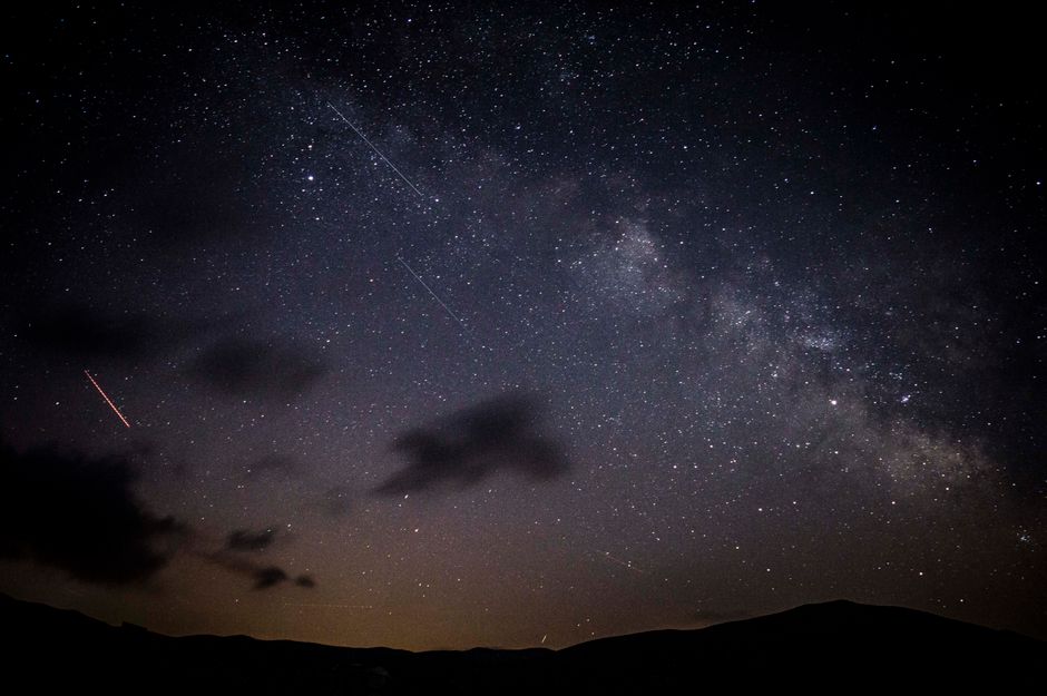 A stunning night sky showcasing stars, clouds, and the Milky Way galaxy with a visible meteor shower.
