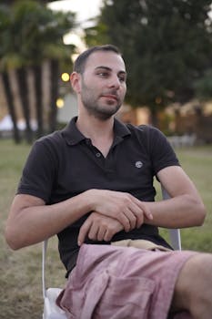 Young man in casual wear sitting outdoors at dusk, enjoying a peaceful moment.