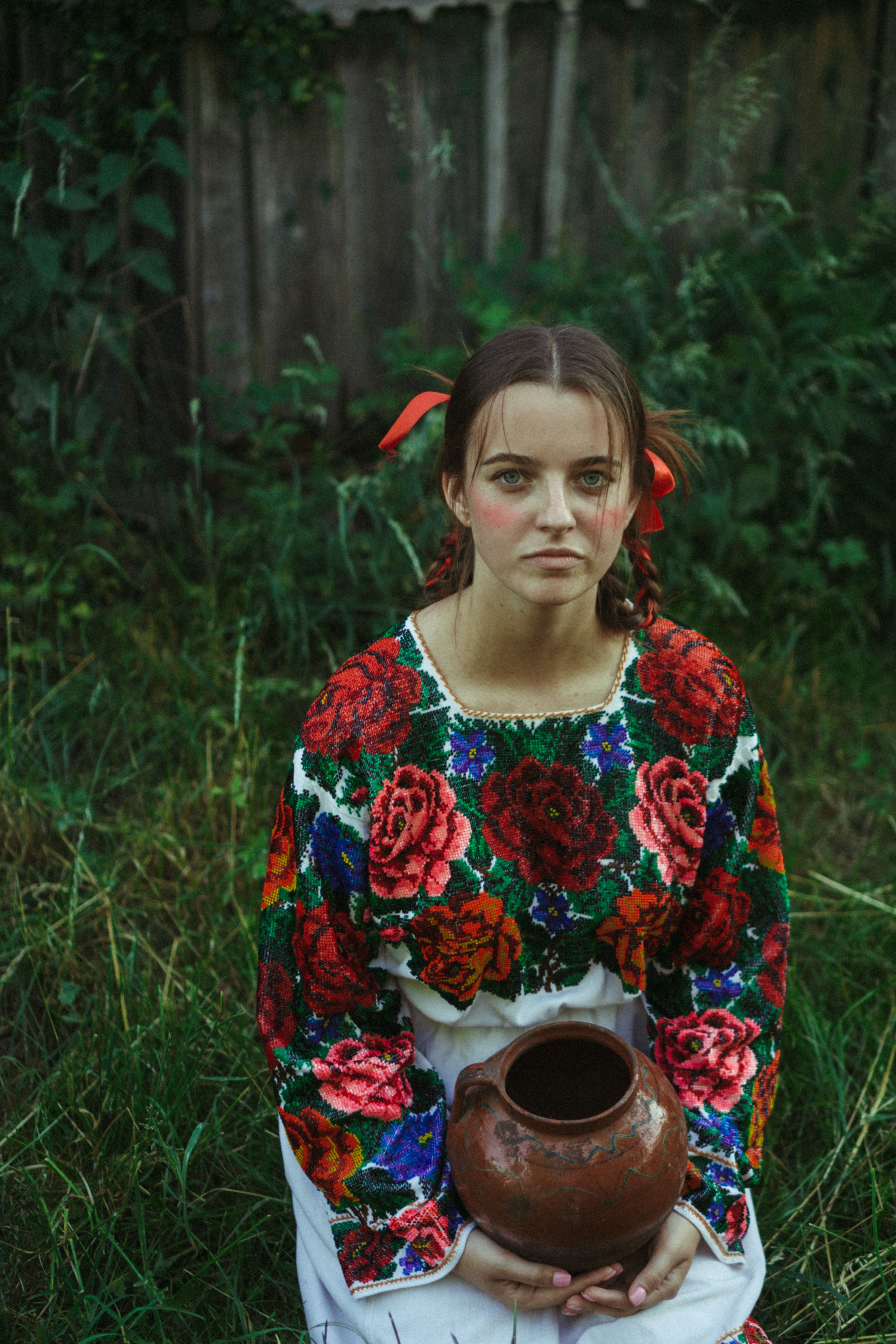 A young woman with long hair in traditional clothing holding a vase outdoors.