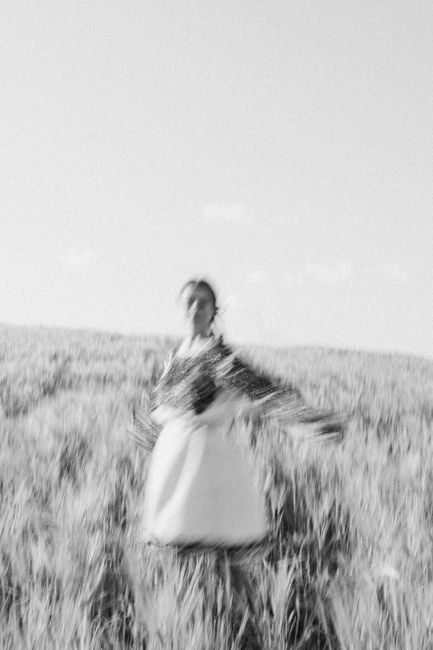 Blurred black and white image of a woman standing in a wheat field, creating a dreamlike effect.