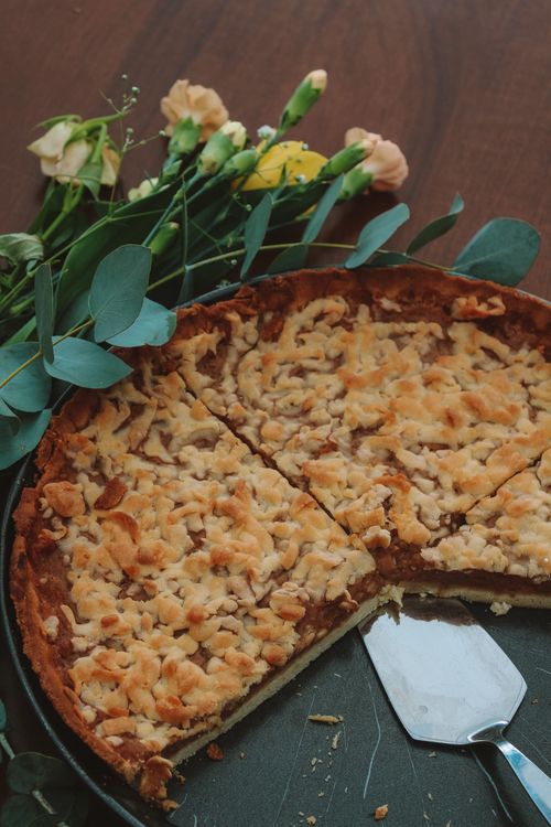 Free Close-up of a freshly baked apple pie next to a floral bouquet on a wooden table. Stock Photo