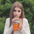 Woman in White Long Sleeve Shirt Holding Jar With Orange Liquid