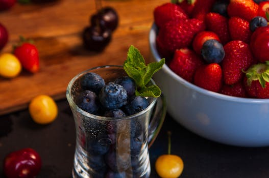 Vibrant assortment of blueberries and strawberries in a glass and bowl, perfect for a refreshing summer snack.