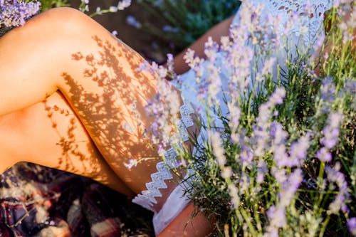Person in White Mini Dress Sitting Beside Purple Flowers with Shadow on Legs