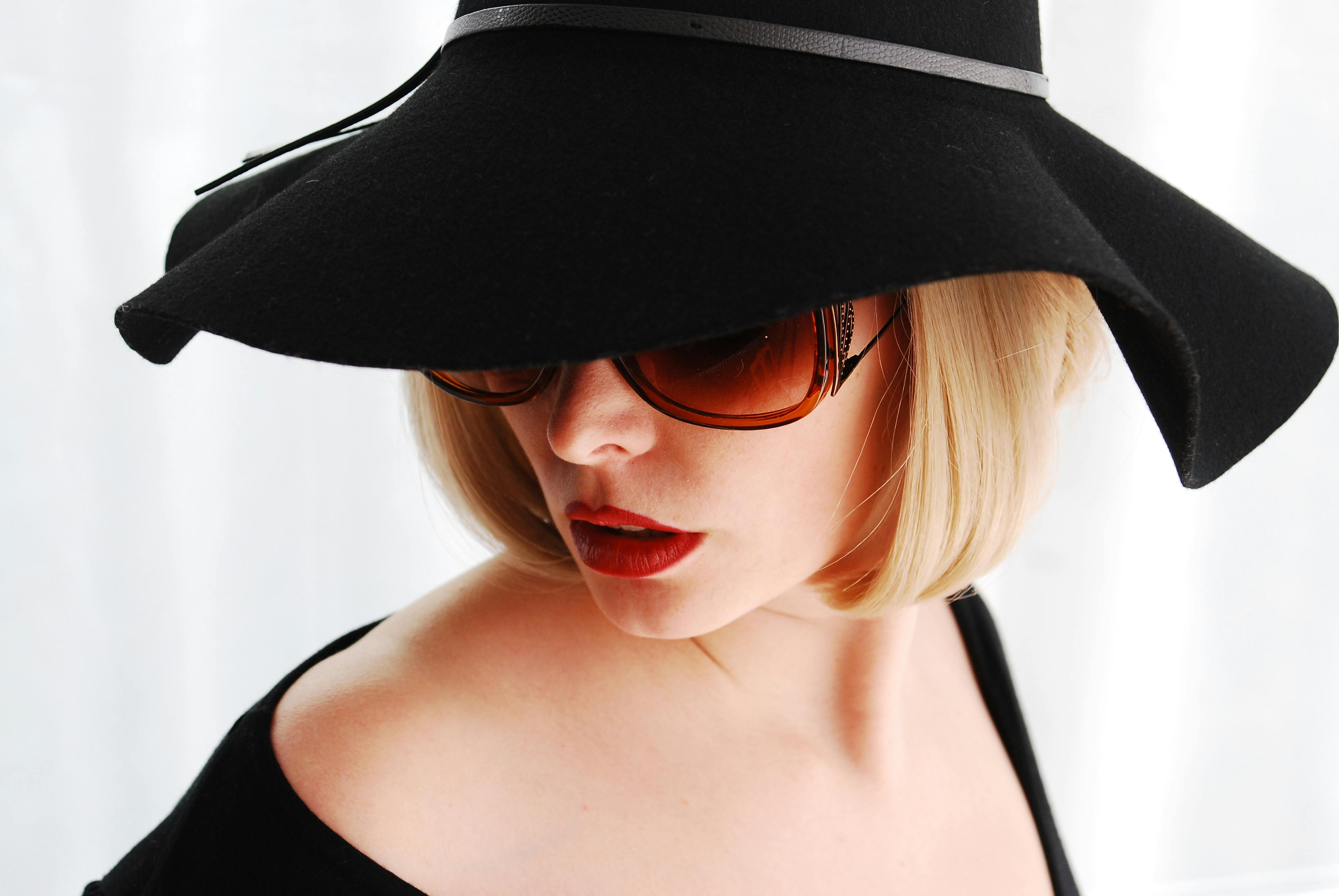 Stylish portrait of a woman in sunglasses and a wide-brimmed hat with a vintage flair.