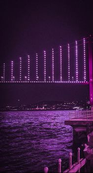 A stunning purple-lit bridge at night over a flowing river with city lights in the background.