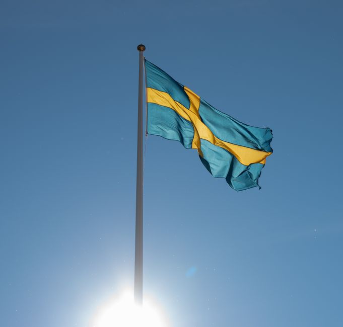 The Swedish flag waves atop a tall flagpole under a bright blue sky, symbolizing national pride.