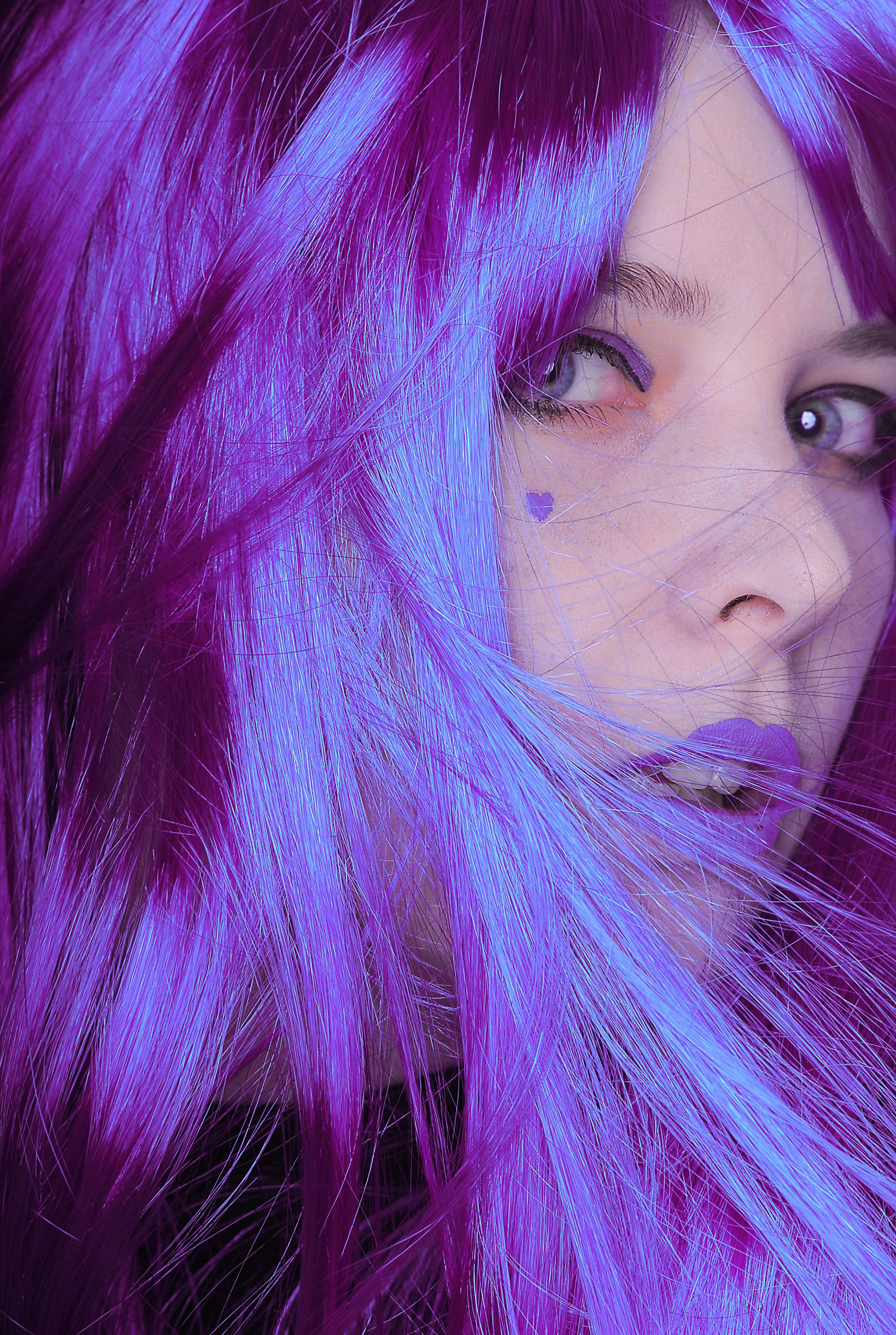 Close-up portrait of a woman with art makeup and vibrant purple hair.