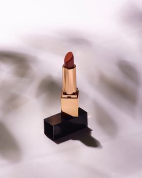 A luxurious red lipstick with gold casing on a white background with shadow effects.