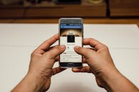 特写一只在室内使用智能手机的手，屏幕上显示着社交媒体页面