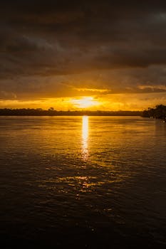 Golden sunset reflecting on calm lake waters with vibrant colors and dramatic clouds.