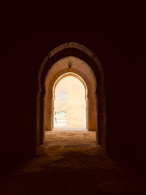 Fotomural Una vista encantadora de un túnel arquitectónico histórico que conduce a un arco iluminado por el sol.
