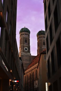 Low angle view of Frauenkirche towers in Munich against a vibrant purple sky at twilight.