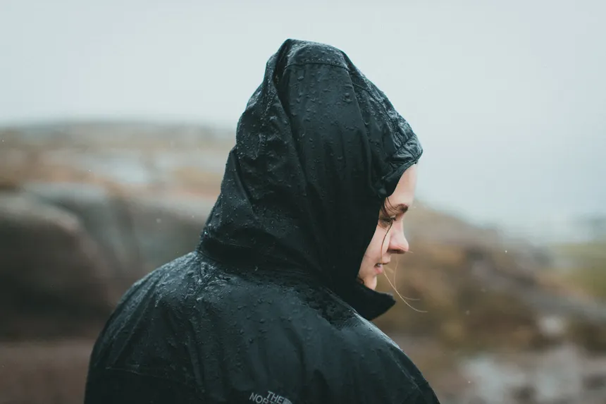 Side view of a woman in a rain jacket outdoors, experiencing rain with serene expression.