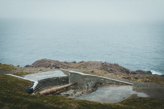Foggy view of a historic military battery by the sea, showcasing rugged coastlines and a serene atmosphere.