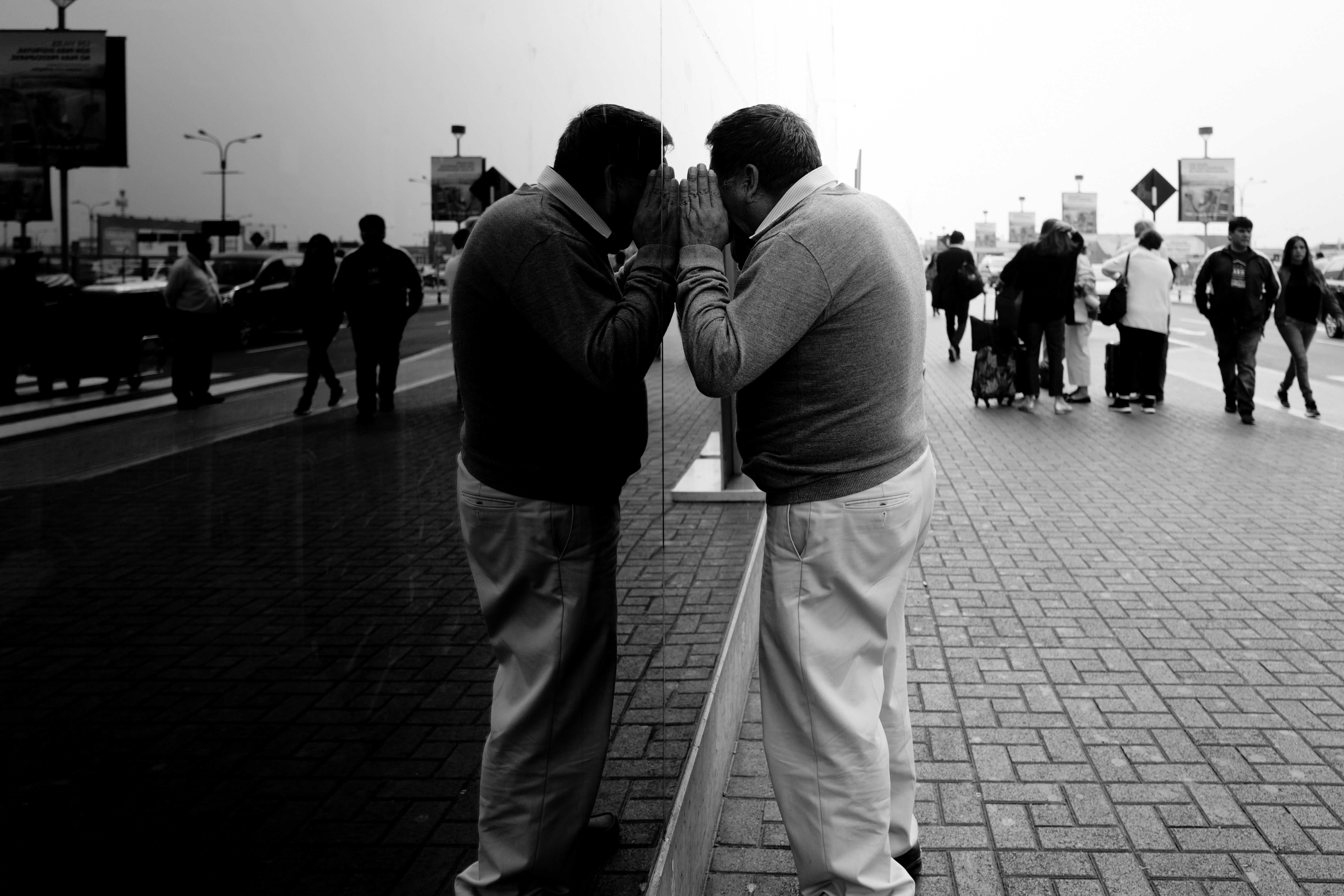 A man peers into a reflection on a glass panel in a bustling Peruvian street.
