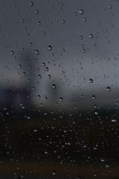 Raindrops on glass with a blurred cityscape in the background, creating a moody atmosphere.