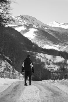 A man stands on a snowy road heading towards mountains in winter, Lëpushë, Albania.