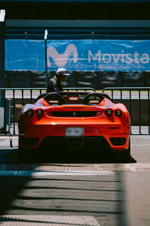 Free Orange Ferrari sports car parked in urban area with metal railing and concrete floor. Stock Photo