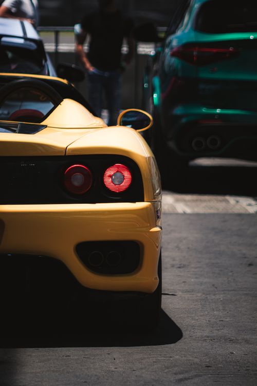 Free Detail view of a yellow sports car parked on an asphalt road with a focus on the rear bumper. Stock Photo