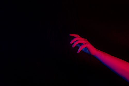 Free Close-up of a hand reaching out in dramatic red and blue lighting on a black background. Stock Photo