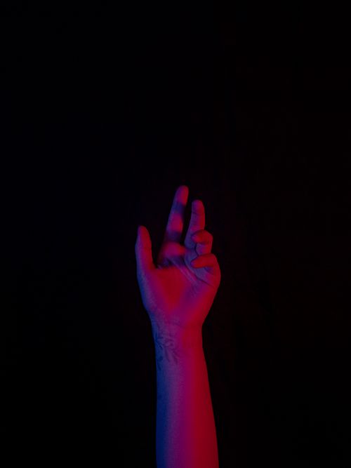 Free A close-up of a hand reaching out in dramatic red and blue lighting against a black background. Stock Photo