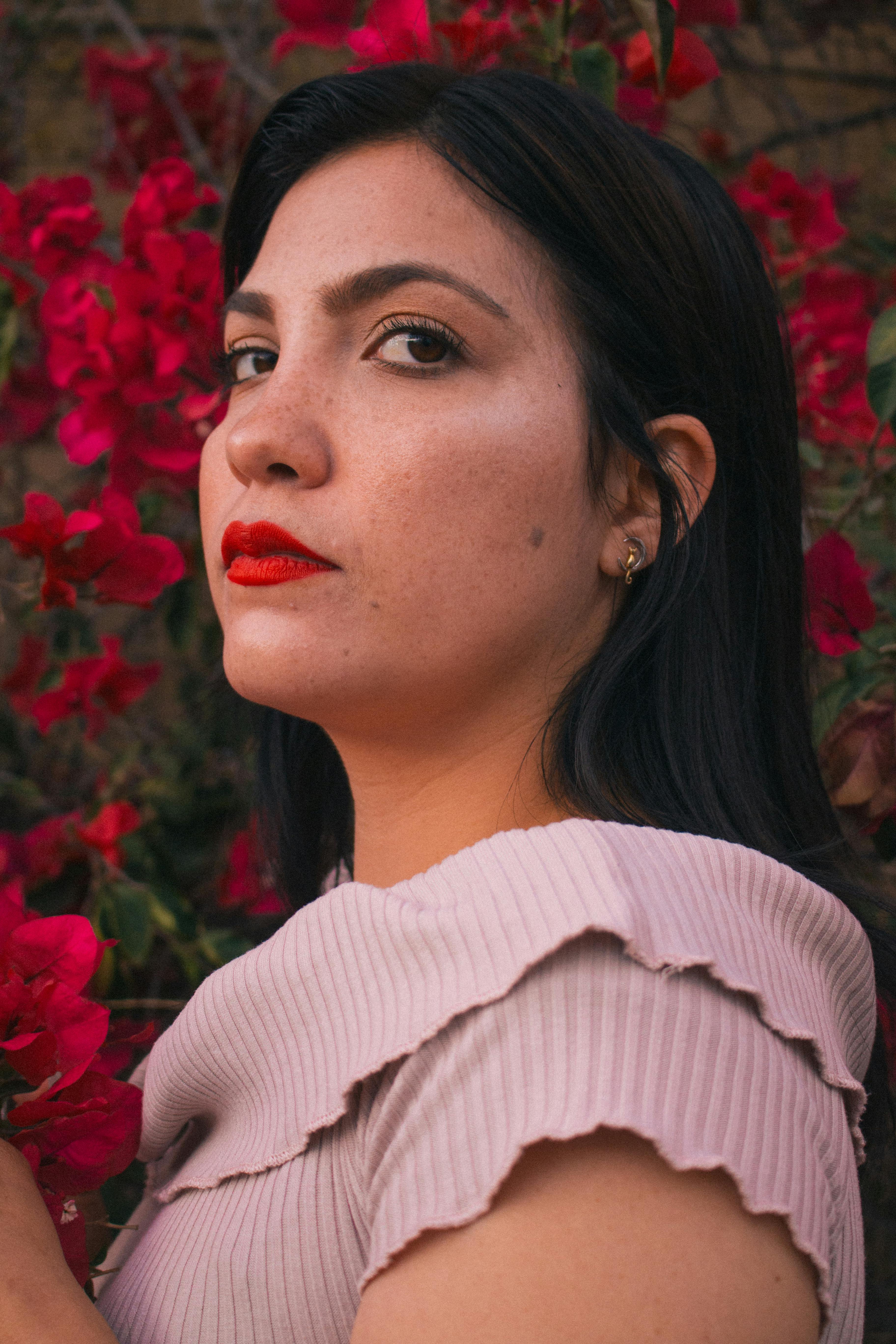 A serene portrait of a woman with vibrant red flowers in the background.