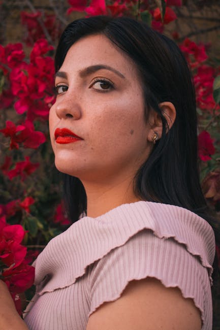 A serene portrait of a woman with vibrant red flowers in the background.