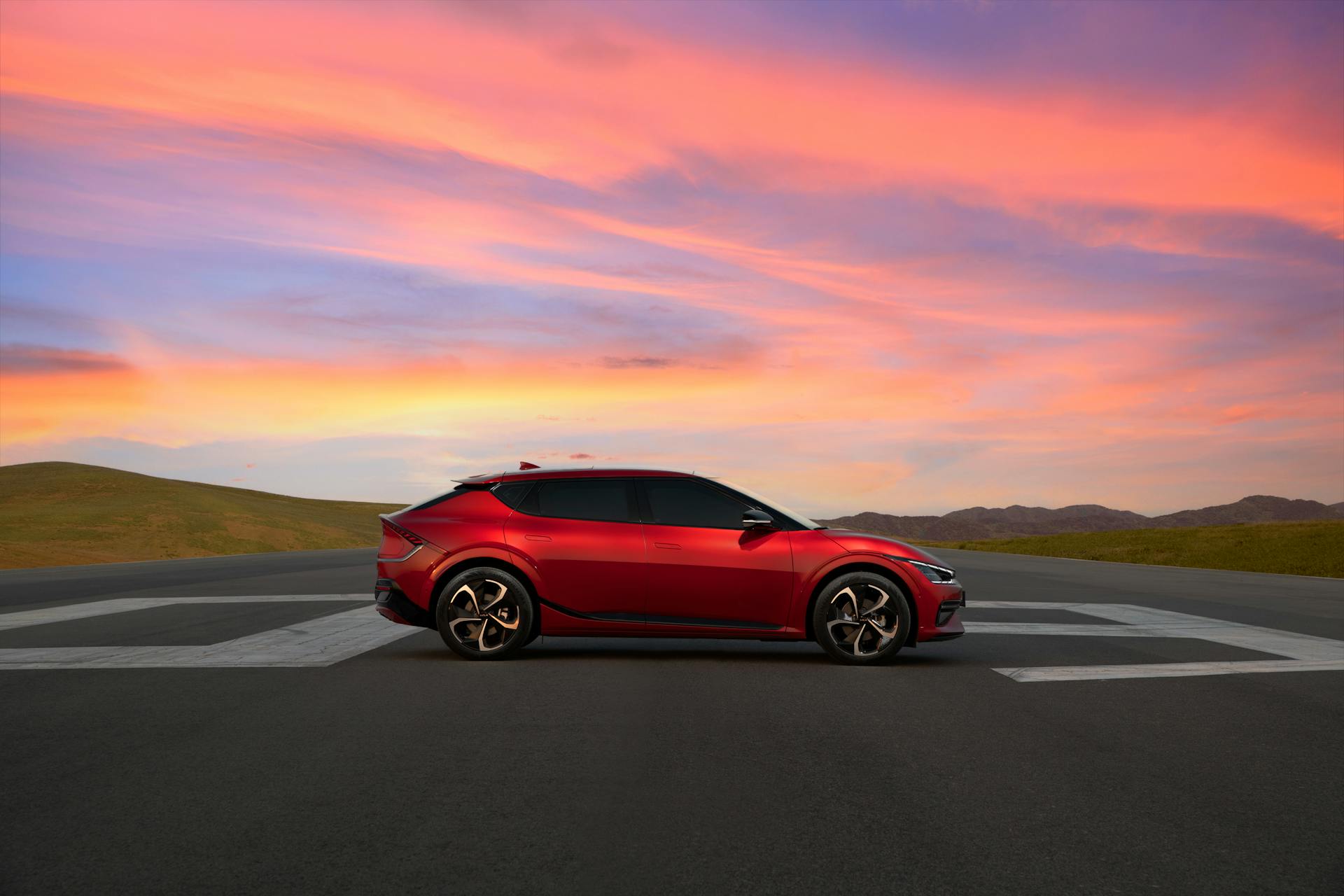 Sleek red electric car parked on a runway with a vibrant sunset sky.