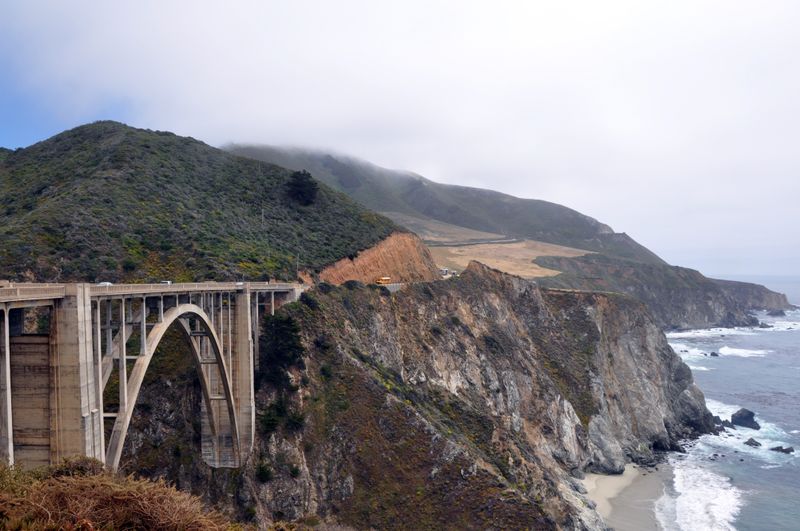 Fog over a coastal bridge with surf breaking against the cliffs — photo by Bobby Mc Gee Lee on Pexels