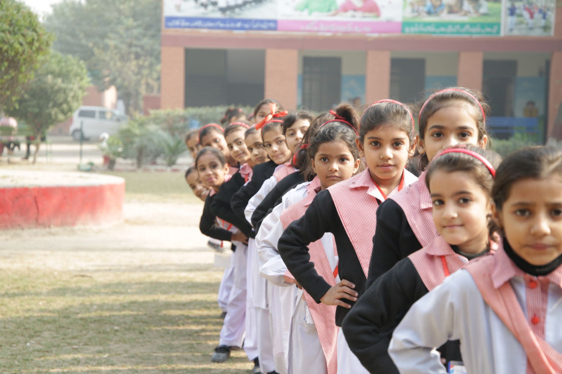 Een groep schoolmeisjes in uniform staat buiten in de rij, met de handen op de heupen, wat eenheid en discipline toont.