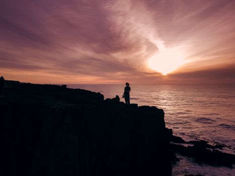 A striking silhouette of a person standing on the cliffs of Depoe Bay during a vibrant sunset.