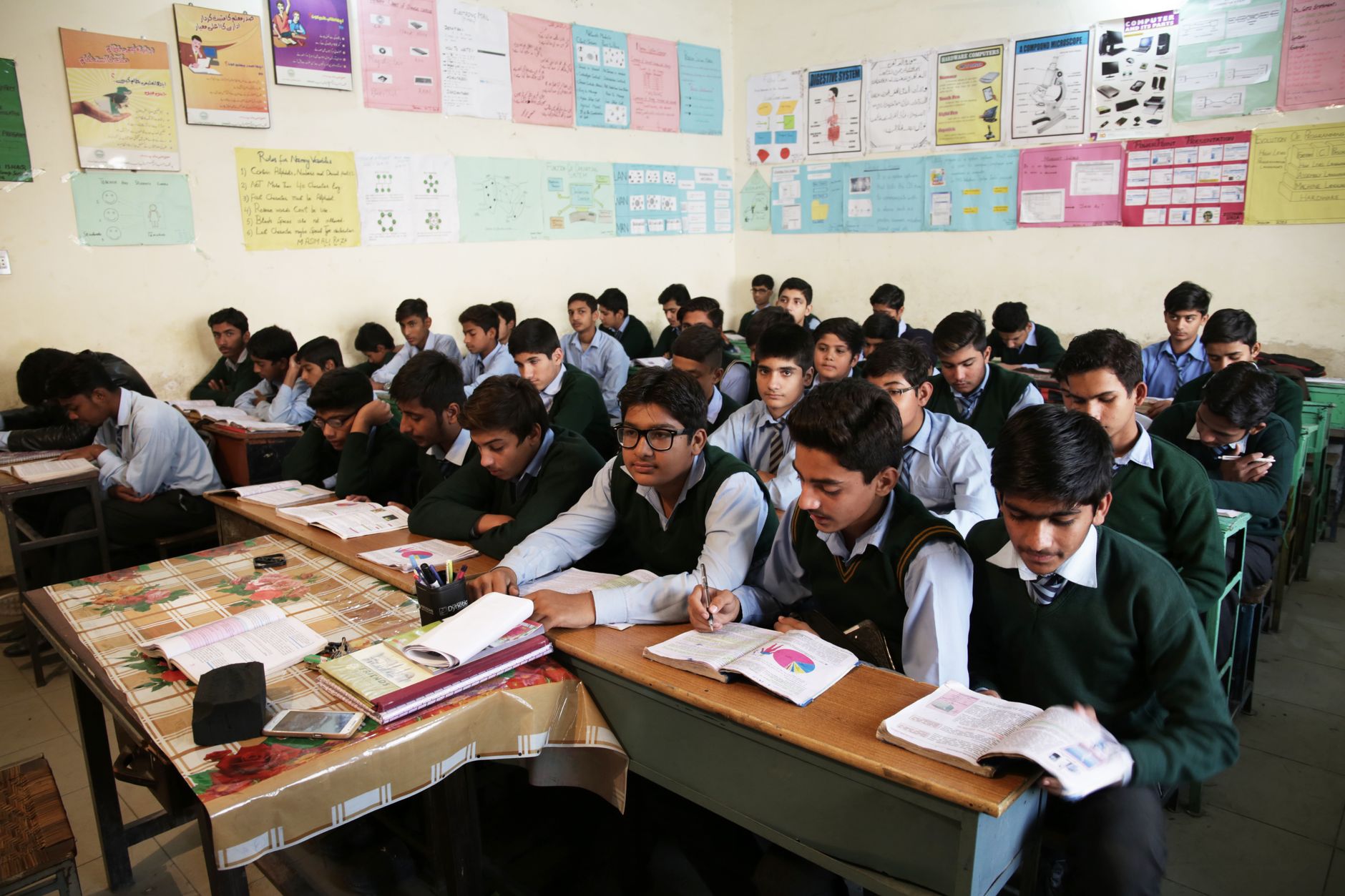 High school boys attentively listening and taking notes in a crowded classroom.