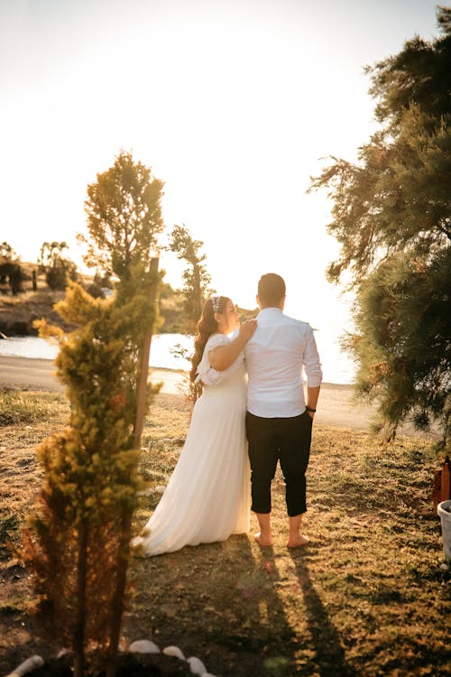 Bride and Groom Standing on Green Grass Near Trees