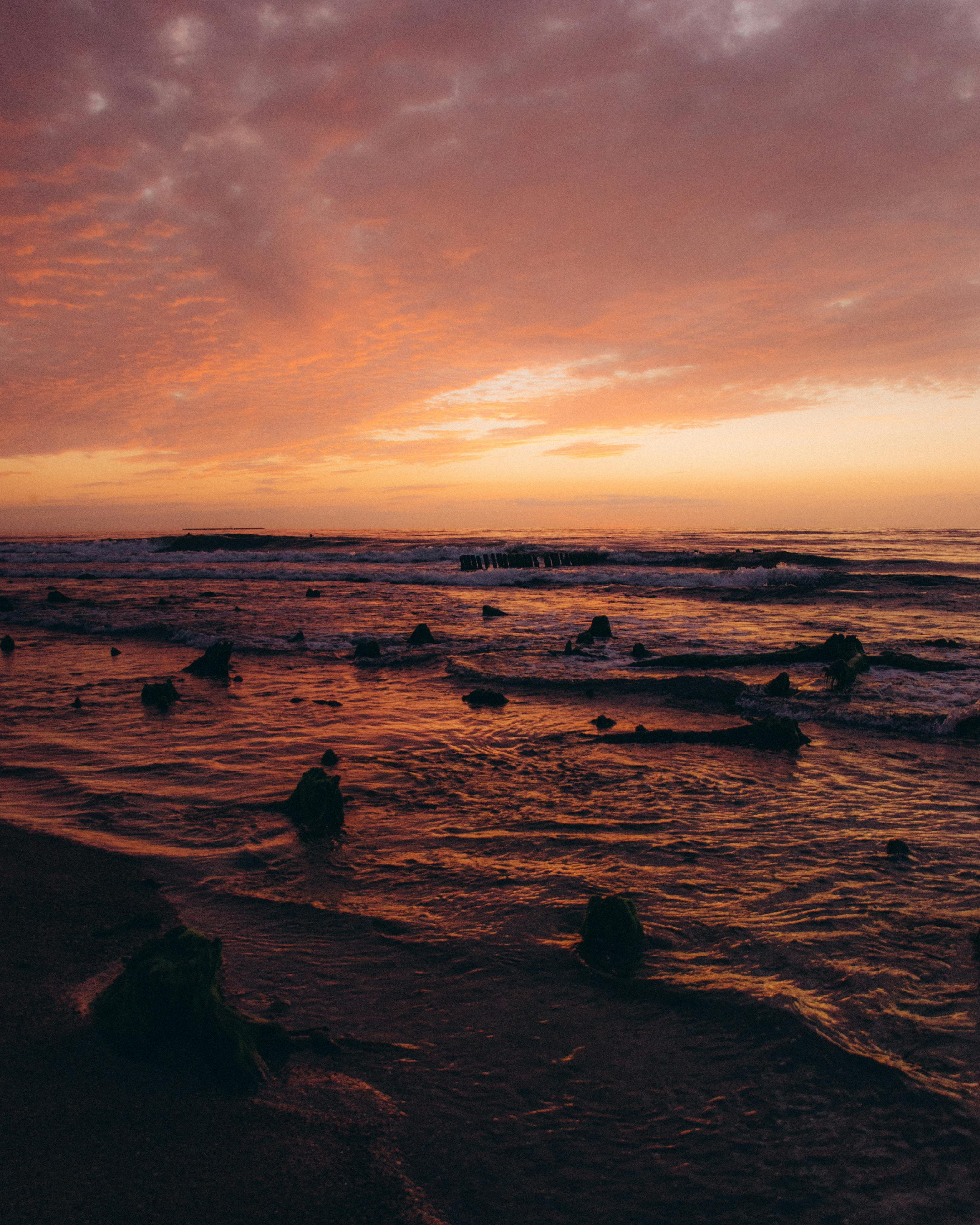 sea waves crashing on rocks and a beach at sunset