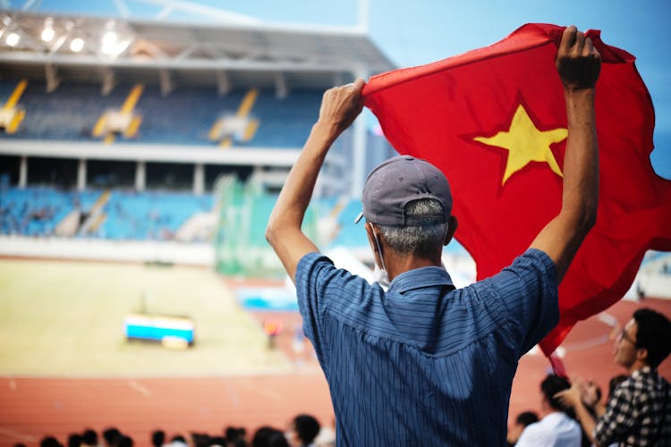 Man Holding Up A Flag At A Stadium 