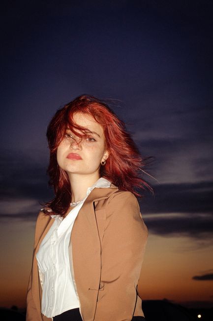 Elegant woman in formal wear against a dramatic dusk sky, exuding confidence and style.