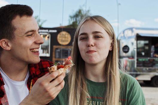 A happy couple enjoying pizza at an outdoor food truck festival, capturing a moment of laughter and joy.