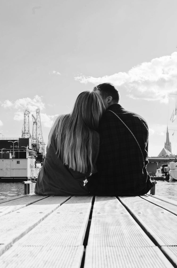 Grayscale Photo Of Couple Sitting On A Dock