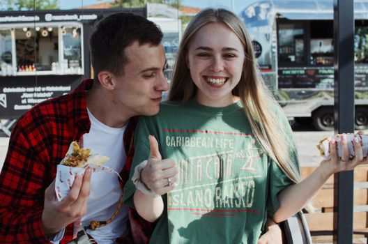 Young couple eating food and enjoying a sunny day at a street food market in Łódź, Poland.