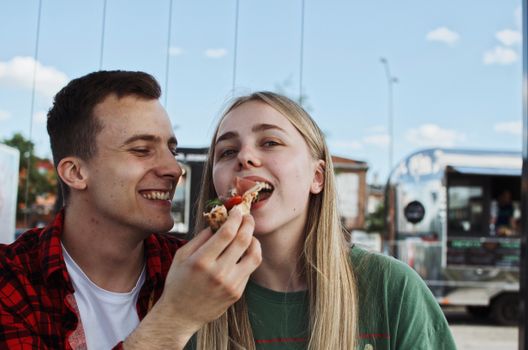 Happy couple sharing street food at an outdoor market, enjoying a sunny day together.