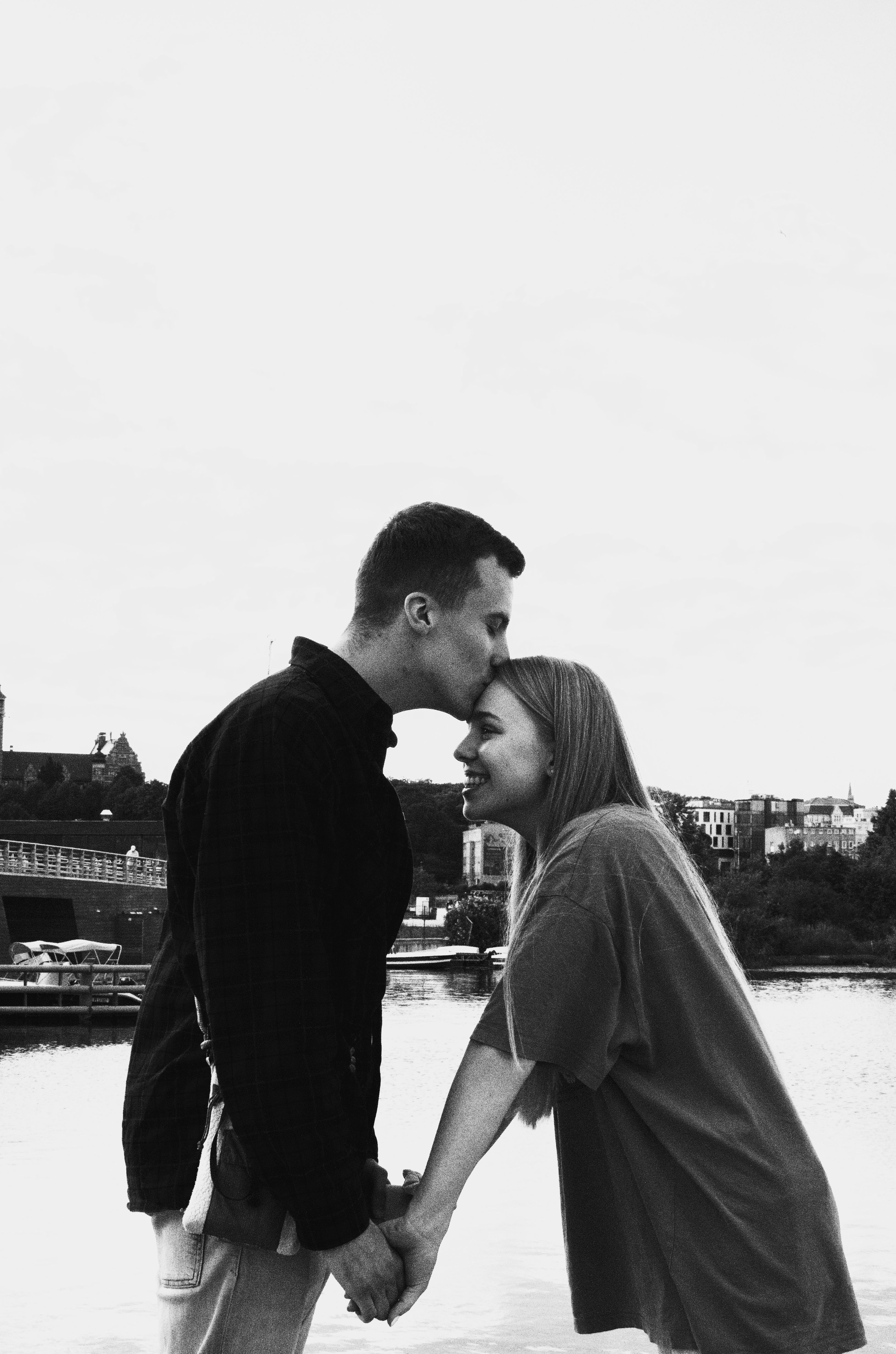 Black and white photo of a couple sharing a tender moment by a river in Gdańsk, Poland.