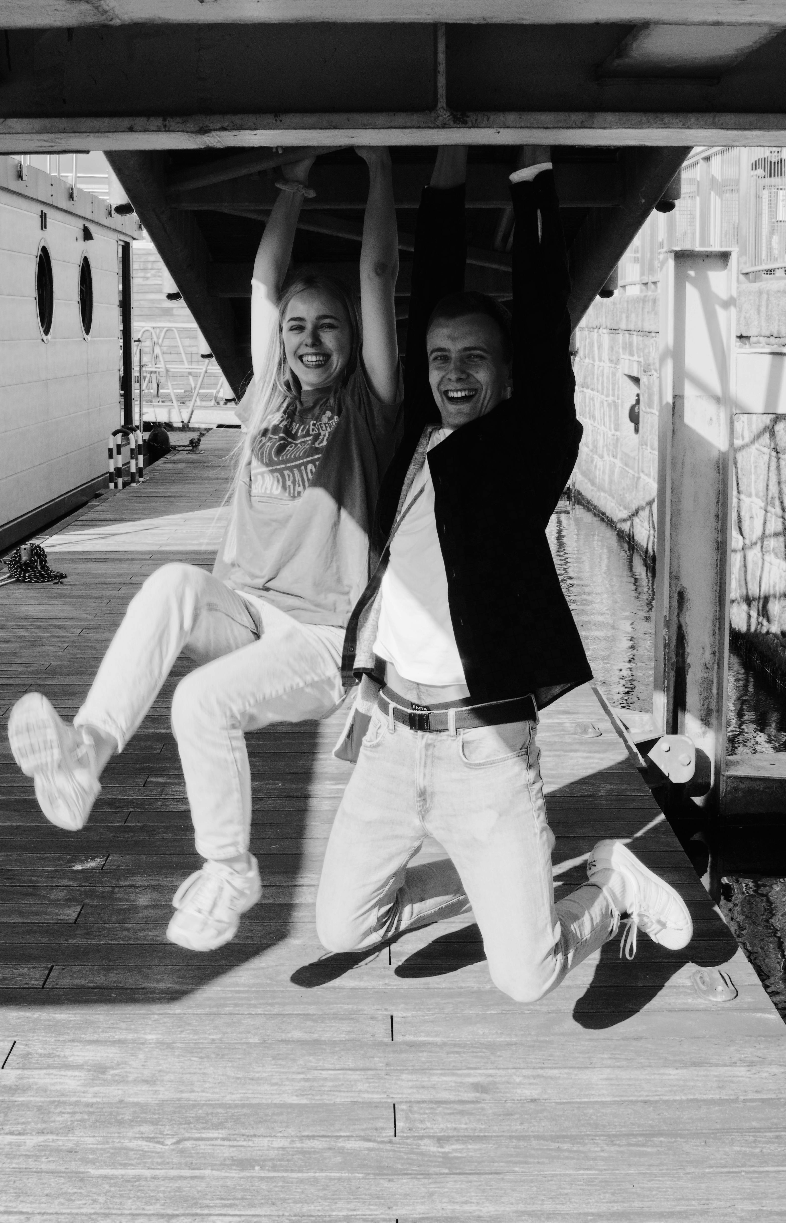 Happy couple joyfully hanging from a structure, sharing a carefree moment in black and white.