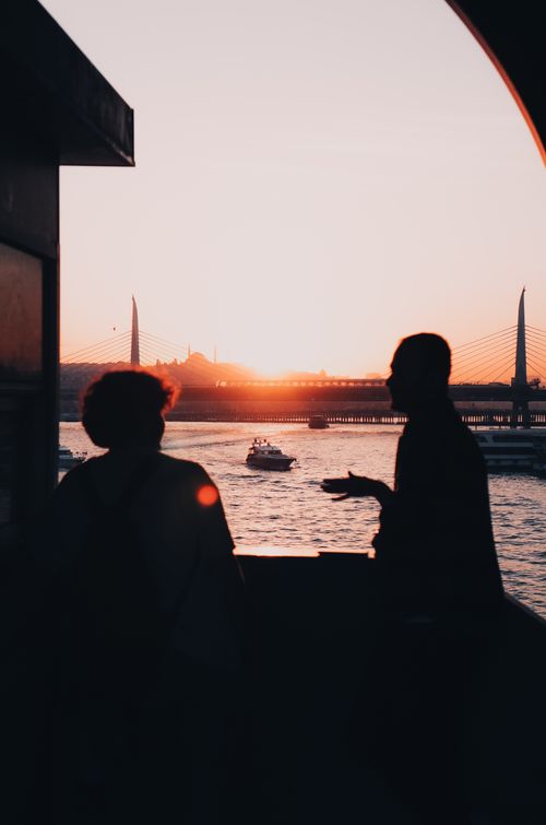 Free Two men silhouetted against the sunset over the Golden Horn in İstanbul, with a boat on the water. Stock Photo